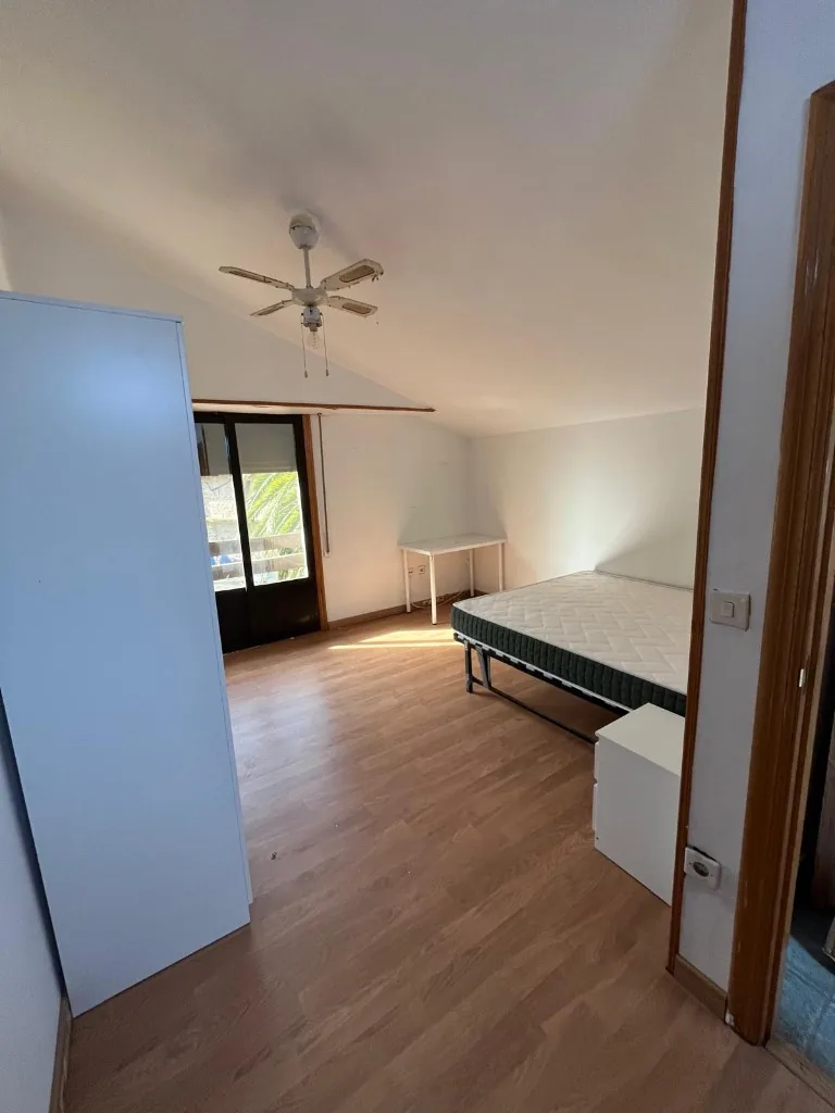 Habitación abuhardillada con armario, cama, mesa y salida al balcón